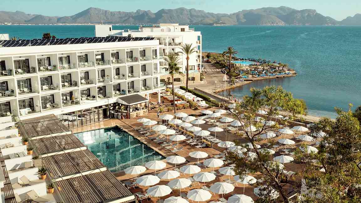 Hotellkompleks ved vannkanten med solsenger og parasoller rundt et basseng. (AI-generert tekst)