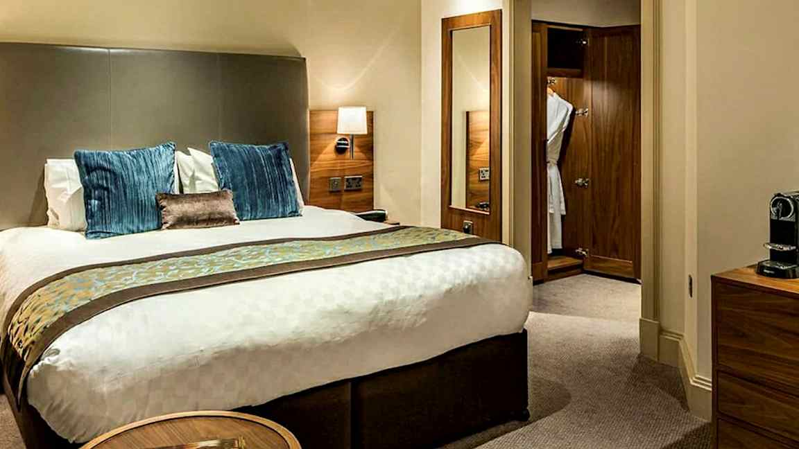 Bilde av et hotellrom med en dobbeltseng, nattbord og garderobe i tre. (AI-generert tekst)