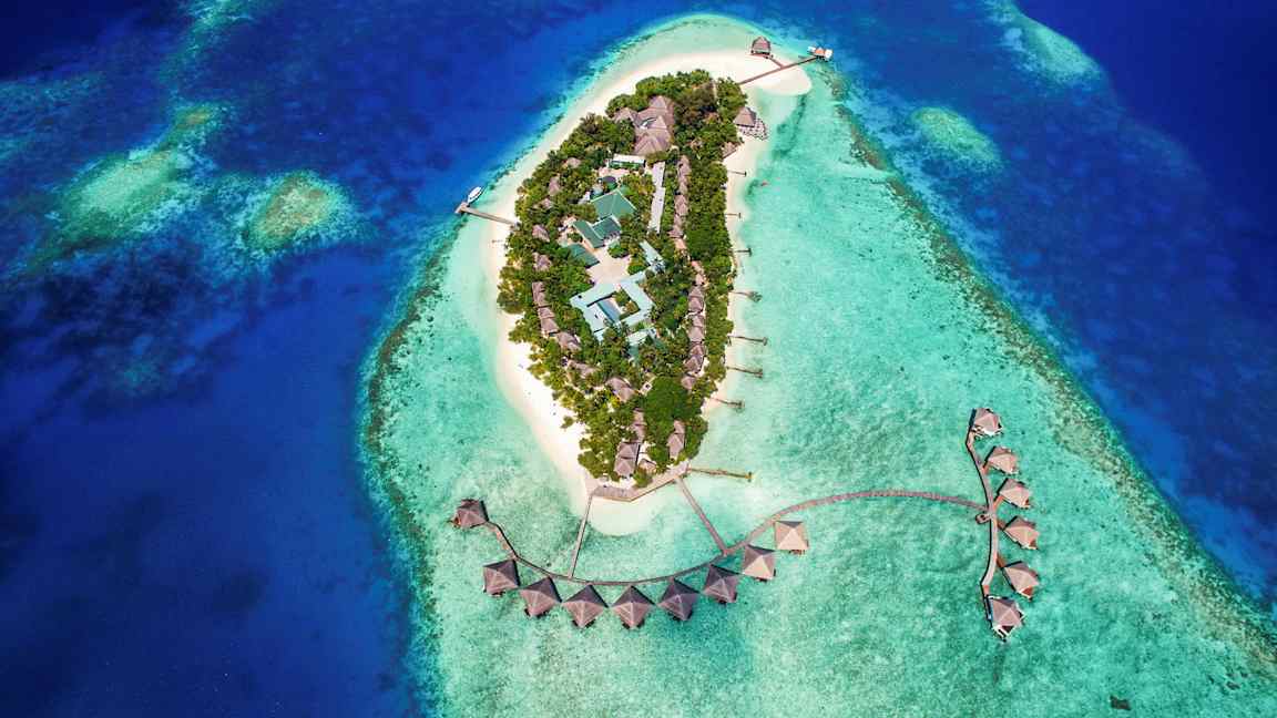 Luftfoto av en tropisk øy med bygninger omgitt av turkist vann. (AI-generert tekst)