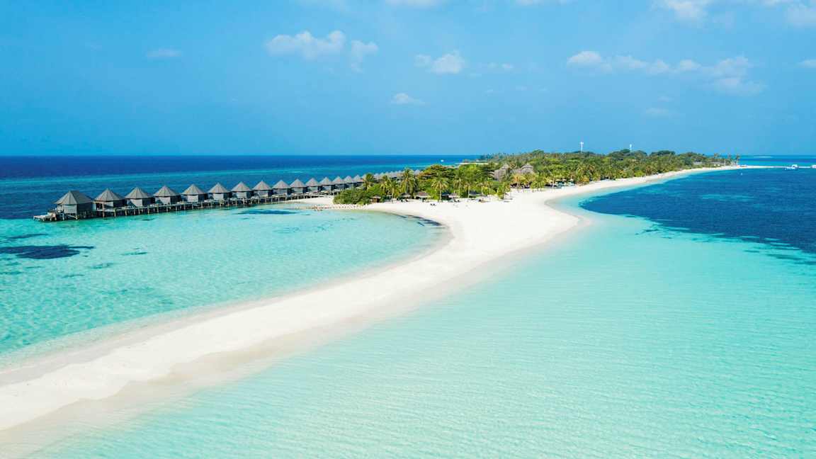 En tropisk strand med klare blått vann, sand og palmer, samt vannbungalower på stylter. (AI-generert tekst)