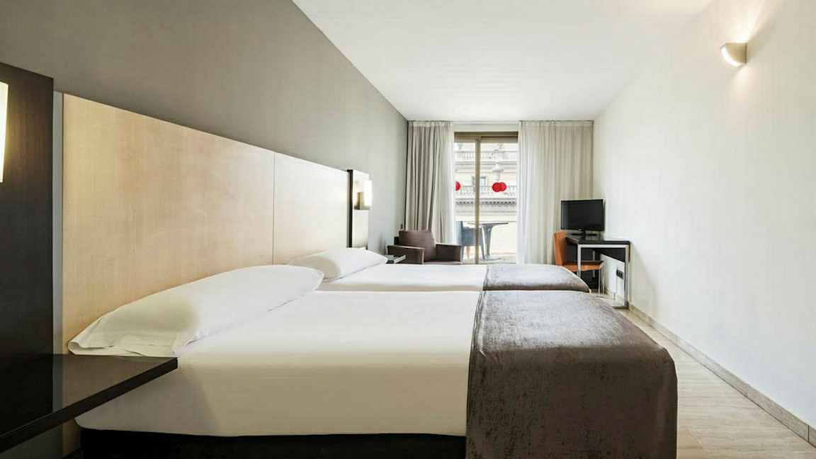 Et hotellrom med to enkeltsenger og et skrivebord ved siden av en balkong. (AI-generert tekst)