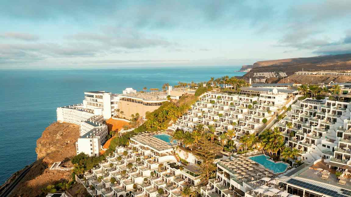 Hotellkompleks på en klippe med bassenger og havutsikt. (AI-generert tekst)