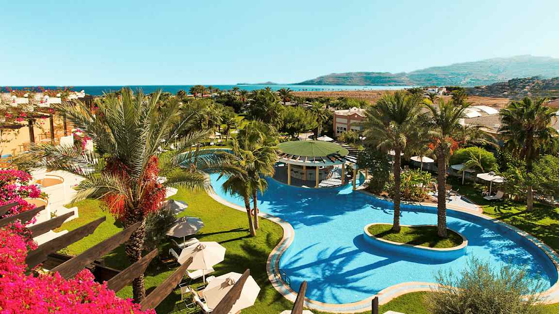 Bilde av hotellområde med et stort basseng og palmer, samt utsikt mot havet. (AI-generert tekst)