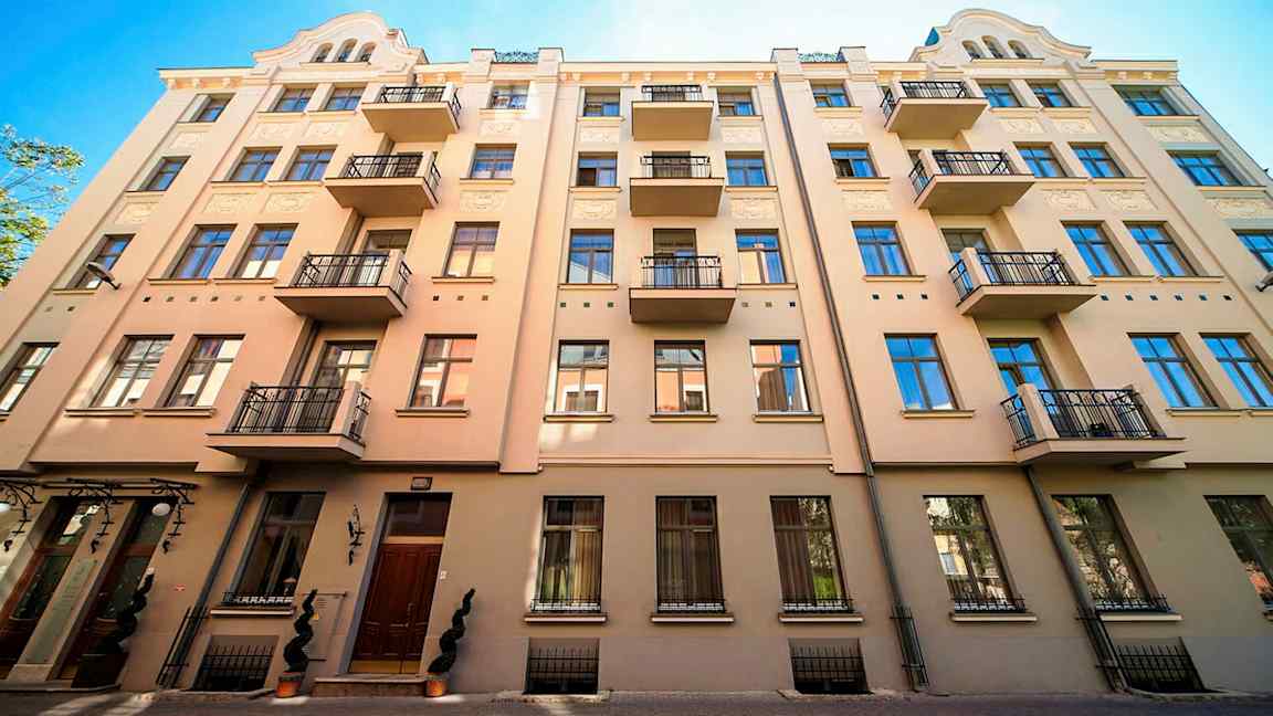 Fasade av en beige bygning med flere balkonger og blå vinduer. (AI-generert tekst)