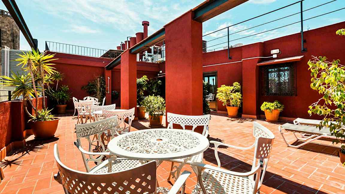 En terrasse med hvite metallmøbler og potteplanter på et teglgulv, omgitt av rødmalt vegger. (AI-generert tekst)