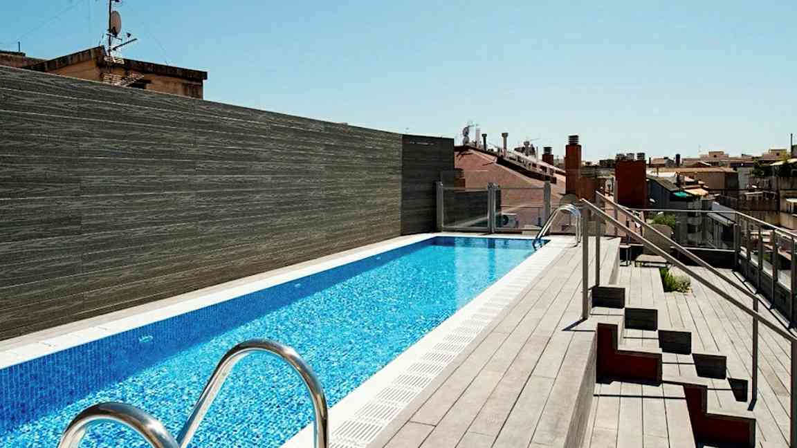 En takterrasse med et langt basseng omgitt av terrassebord og noen sitteplasser på siden. (AI-generert tekst)