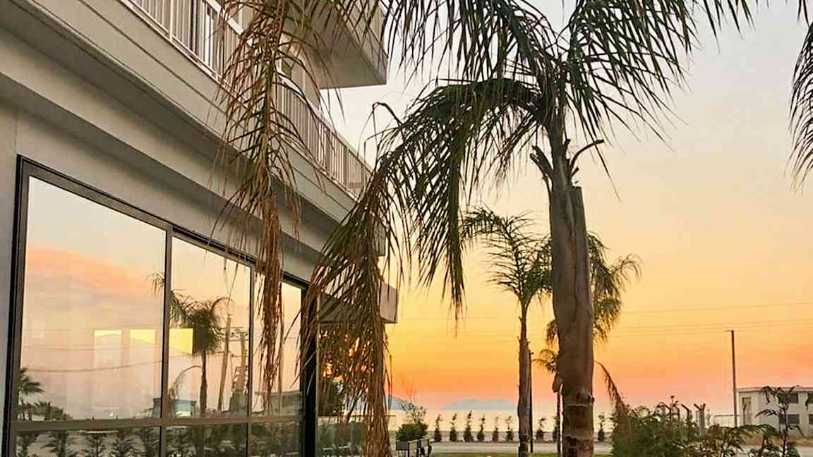 En bygning med glassvinduer og palmer i forgrunnen ved solnedgang. (AI-generert tekst)