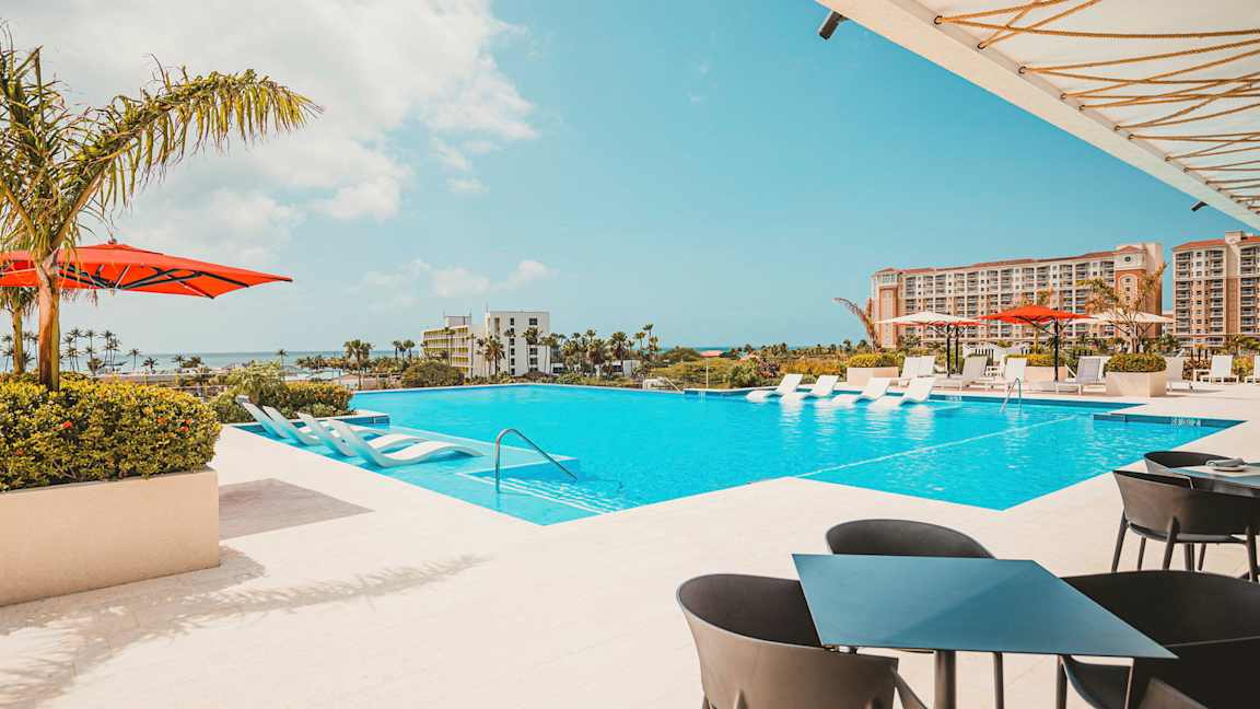 Utendørsbasseng med solsenger og hotellet i bakgrunnen. (AI-generert tekst)