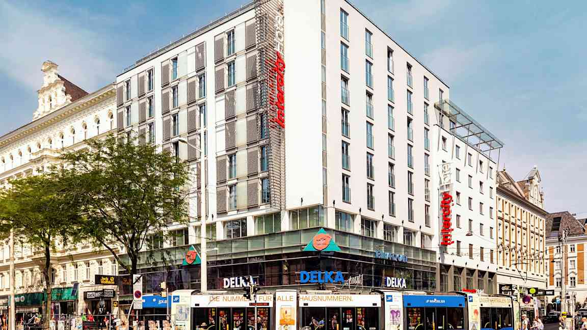 En flerfarget trikk foran et moderne hotell i bymiljø. (AI-generert tekst)