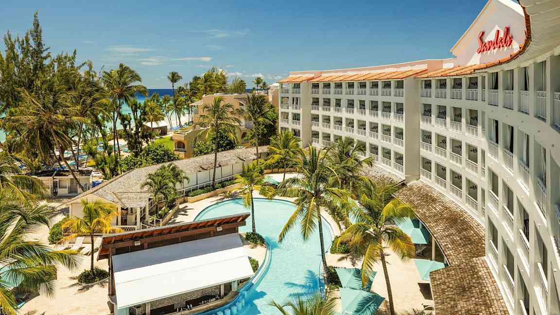 Et hotell med basseng, omkringliggende palmer og nærliggende strand. (AI-generert tekst)