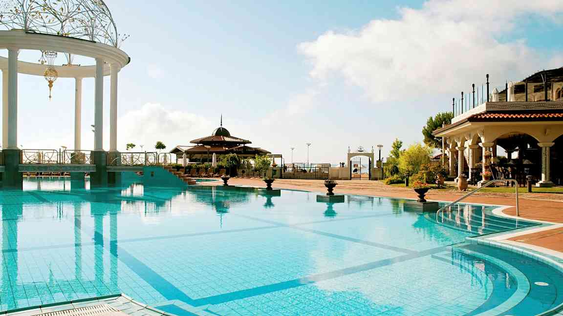 Et utendørsbasseng med en dekorert paviljong og omgivelser med bygninger i middelhavsstil. (AI-generert tekst)