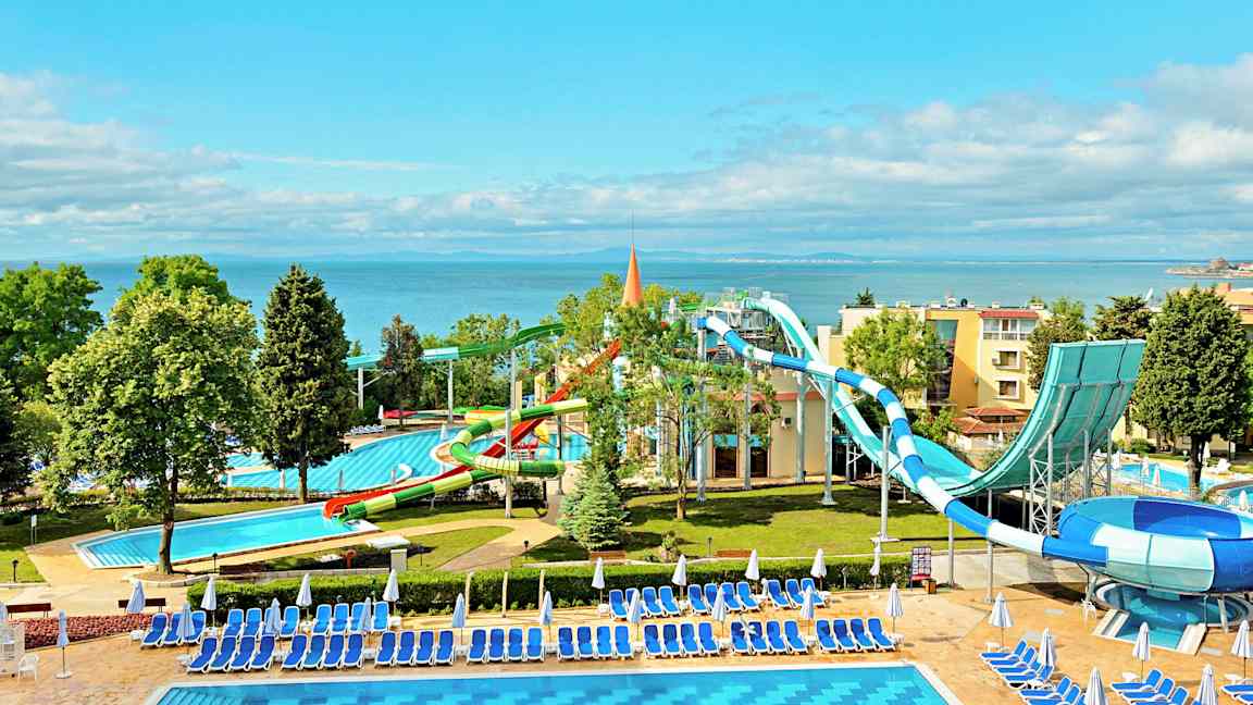 En vannpark ved sjøen med vannsklier og bassenger omgitt av solsenger og parasoller. (AI-generert tekst)