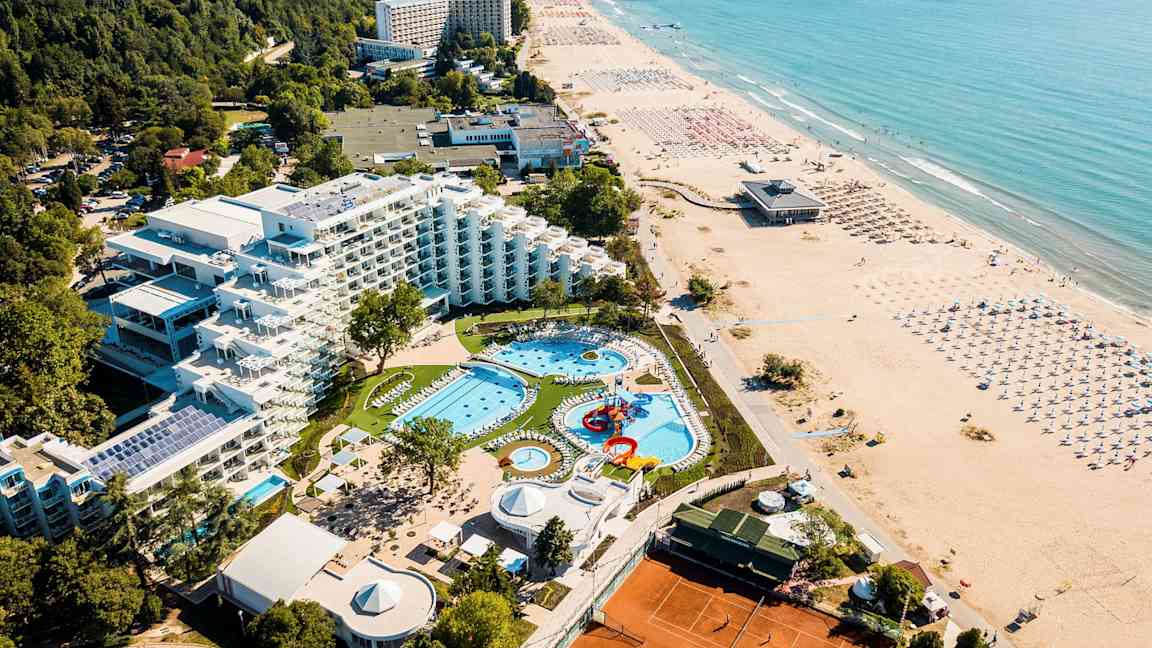 Luftfoto av hotell med bassengområde, grøntområde og strand. (AI-generert tekst)