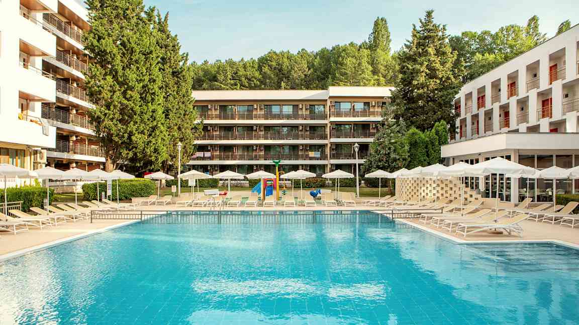 Utendørsbasseng med solsenger og parasoller, omgitt av moderne bygninger og grøntområder. (AI-generert tekst)