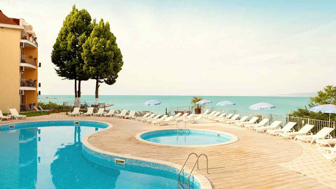 To bassenger med solsenger og parasoller på et sted nær sjøen. (AI-generert tekst)