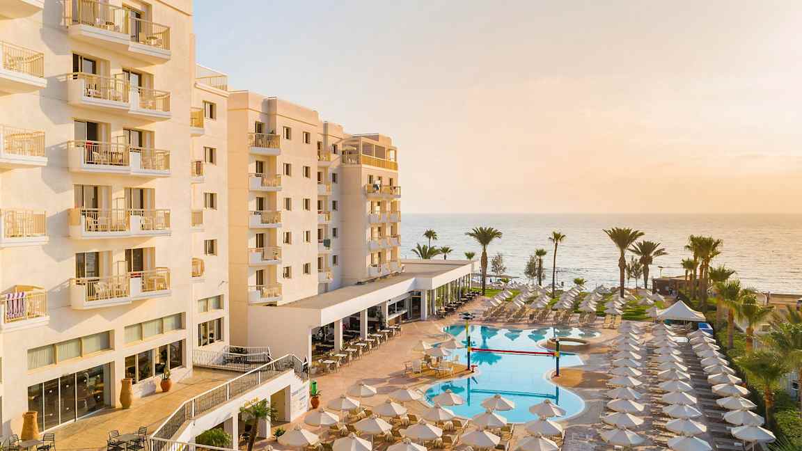 Hotellbygning med balkonger, basseng og solsenger ved stranden. (AI-generert tekst)