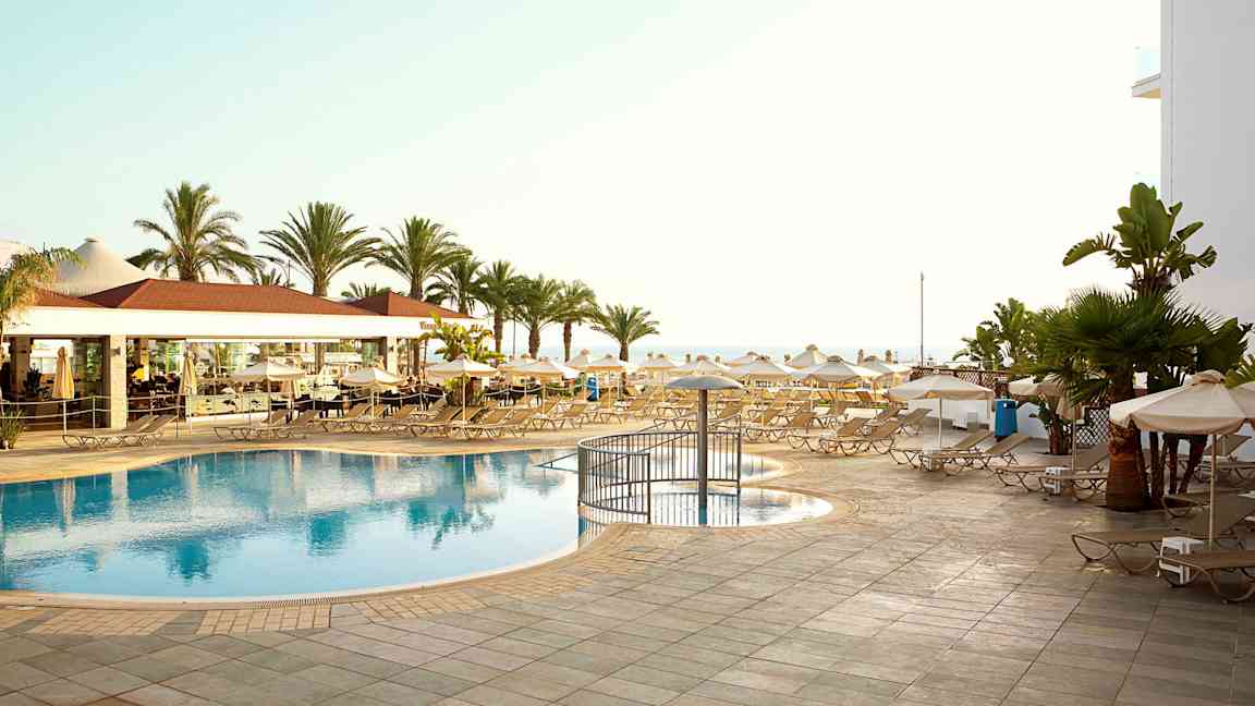 Bilde av et bassengområde med solsenger, parasoller og palmer. (AI-generert tekst)