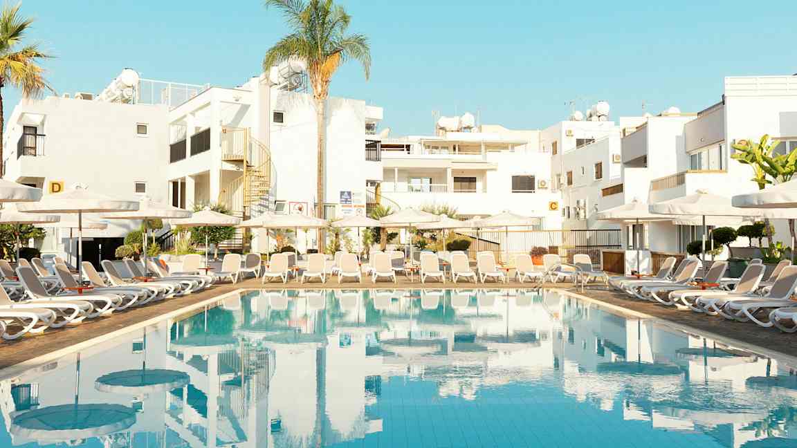 Basseng med solsenger og bygninger i bakgrunnen. (AI-generert tekst)