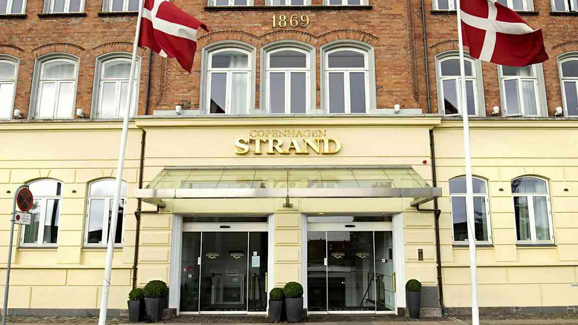 Hotellfasade med skilt som sier 'Copenhagen Strand'. Danske flagg sees ved inngangen. (AI-generert tekst)
