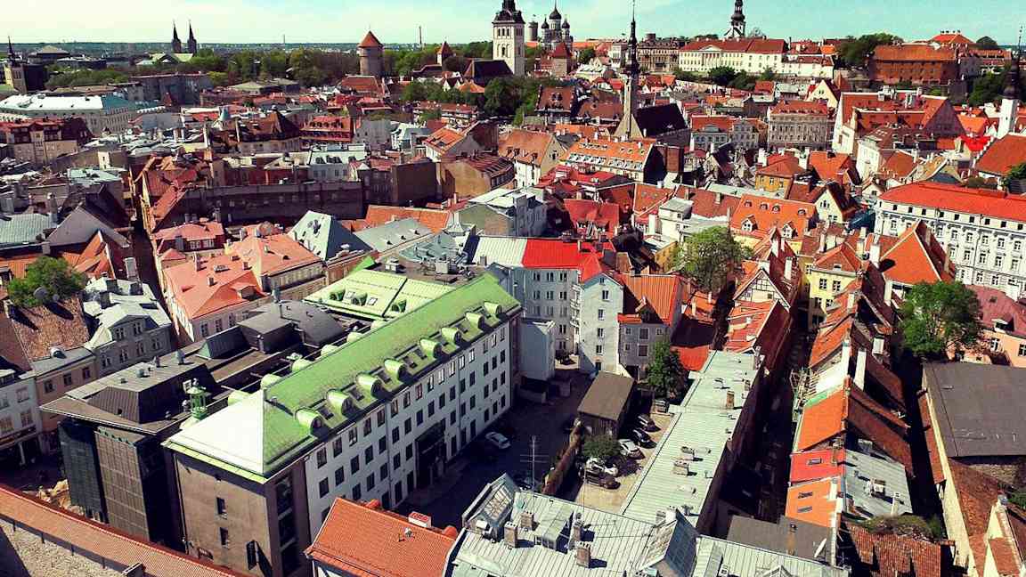 Flyfoto av en by med eldre bygninger i forskjellige farger. (AI-generert tekst)