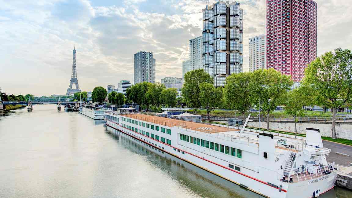 Elv med en båt ved kai, moderne bygninger og Eiffeltårnet i bakgrunnen. (AI-generert tekst)