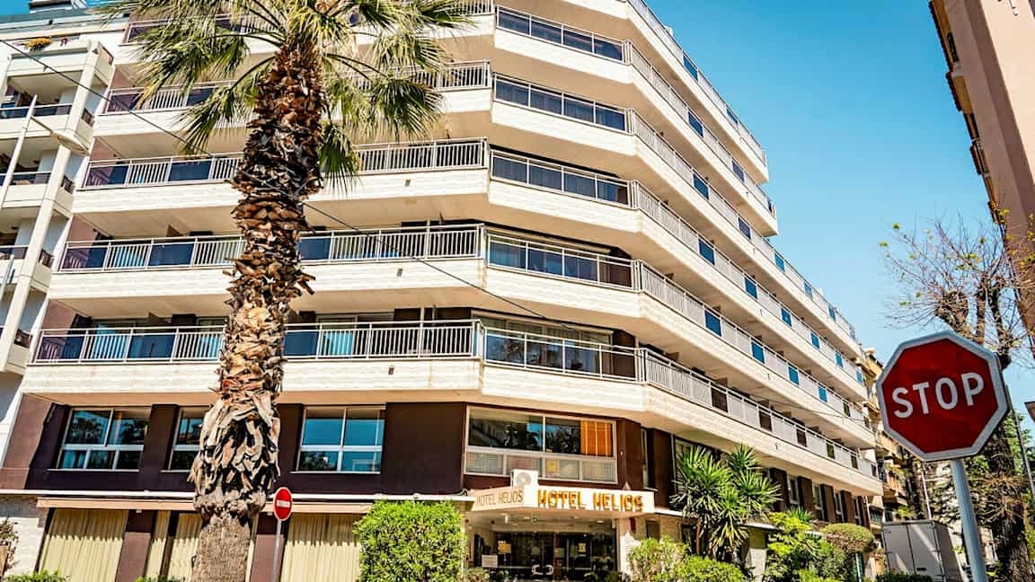 Et hotell med flere etasjer og et palmetre foran. Skiltet "STOP" er synlig til høyre. (AI-generert tekst)