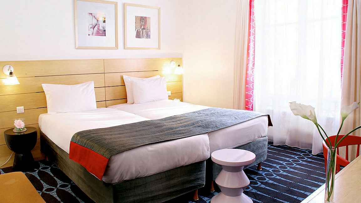 Et hotellrom med to enkeltsenger, et dekorativt sengegavl og et vindu med lysinnslipp. (AI-generert tekst)