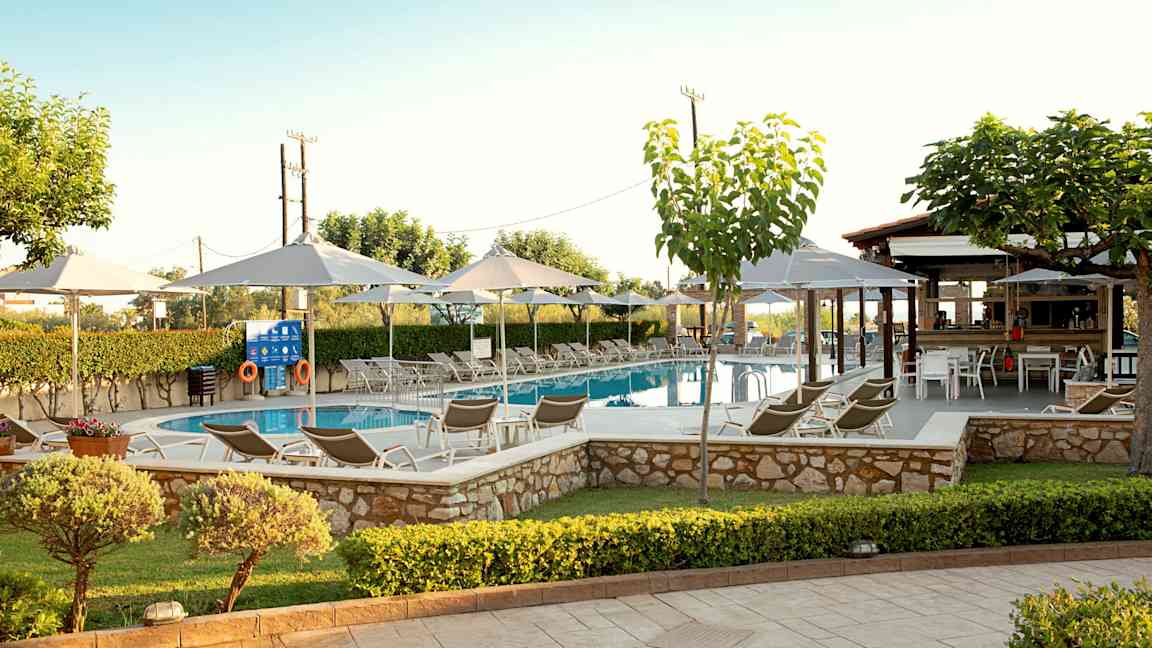 Et svømmebasseng omgitt av solsenger, parasoller og grønne planter. (AI-generert tekst)