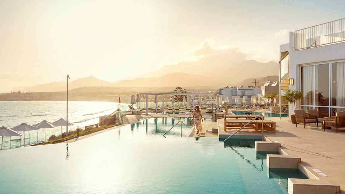 En kvinne ved et infinitybasseng med havet og en fjellkjede i bakgrunnen. (AI-generert tekst)