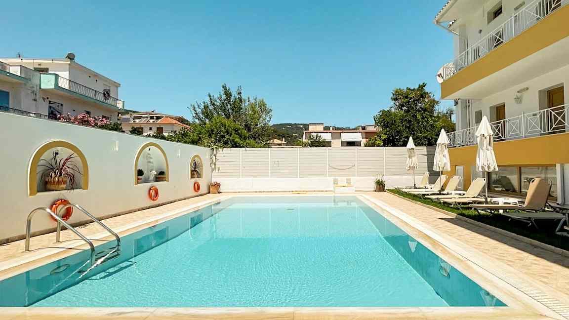 Bilde av et utendørs svømmebasseng omringet av solsenger og bygninger. (AI-generert tekst)