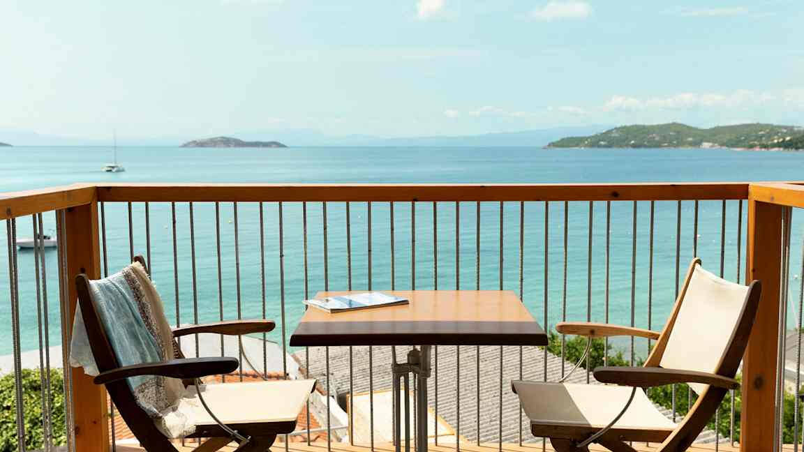 Utsikt fra en balkong med to stoler, et bord og havet i bakgrunnen. (AI-generert tekst)