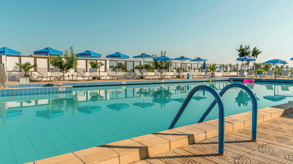 Et bilde av et utendørs basseng med blå parasoller og solsenger rundt. (AI-generert tekst)