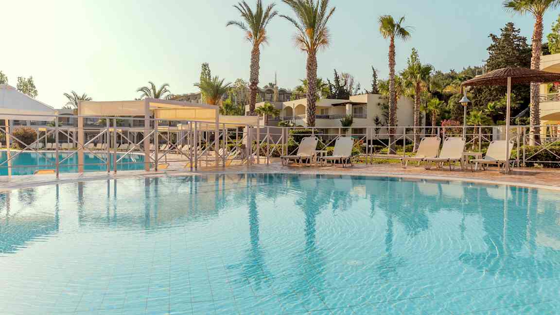 Bassengområde med solsenger og parasoller, omgitt av palmer og bygninger. (AI-generert tekst)