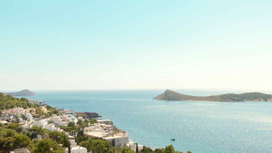 Utsikt over kystlinje med hvite bygninger og grønne trær, havet og en øy i bakgrunnen. (AI-generert tekst)