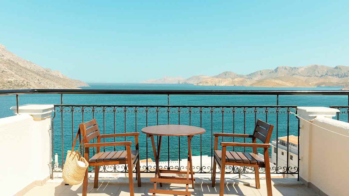 To trestoler og et bord på en terrasse med utsikt over havet og fjell i det fjerne. (AI-generert tekst)