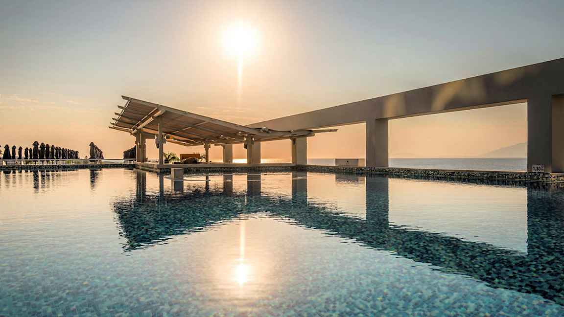 Et svømmebasseng med utsikt over havet og en soloppgang. (AI-generert tekst)