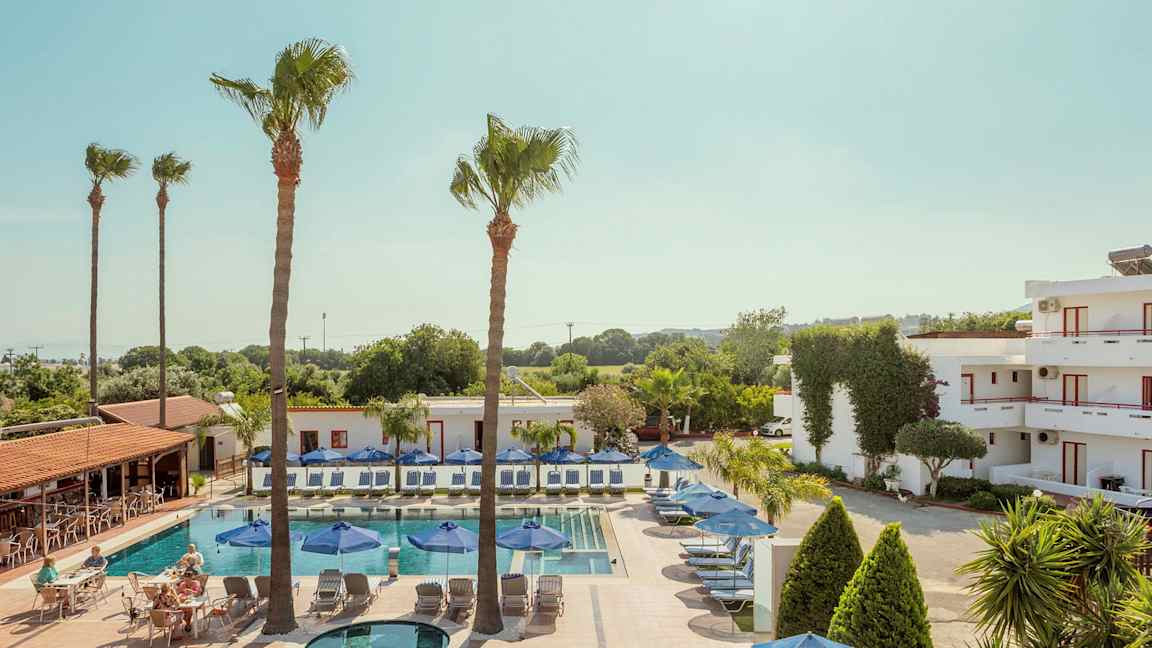 Et basseng med solsenger og parasoller omgitt av bygninger og trær. (AI-generert tekst)