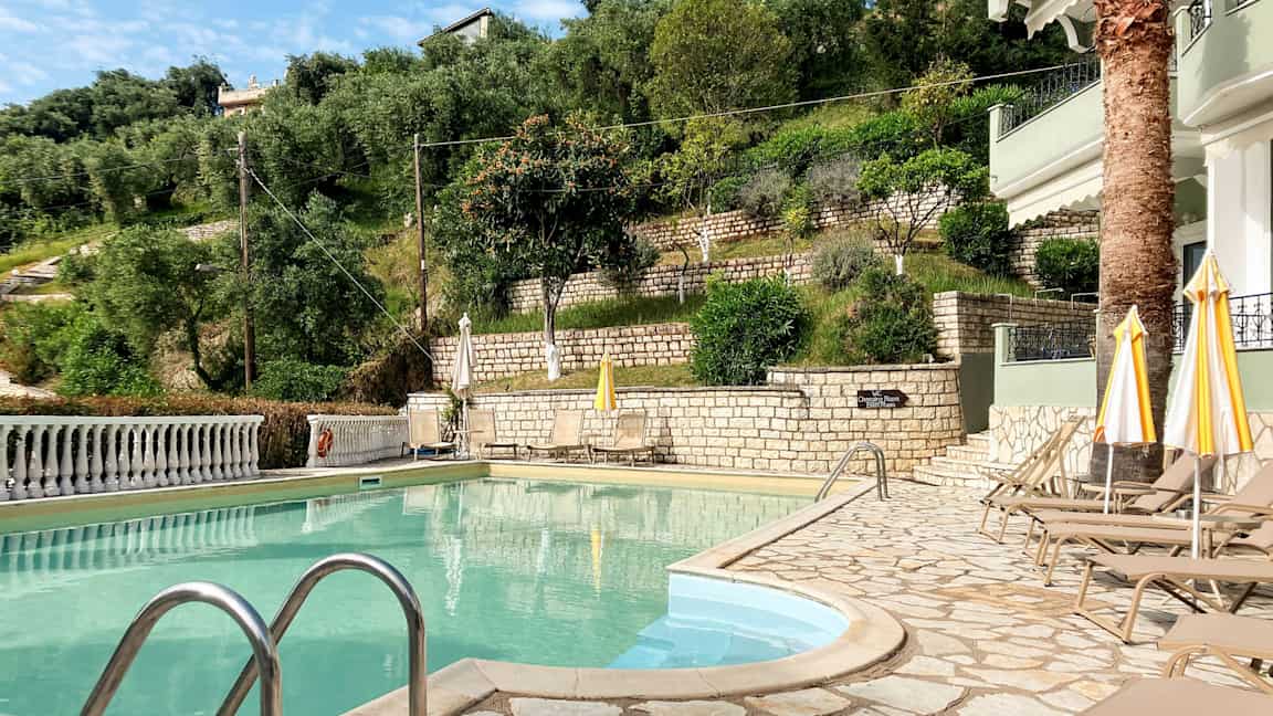 Bilde av et bassengområde med solsenger og parasoller ved siden av en skråning med grøntområder og steinmurer. (AI-generert tekst)