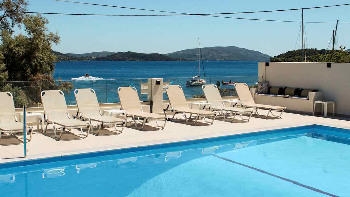 Svømmebasseng med solsenger og havutsikt i bakgrunnen. (AI-generert tekst)