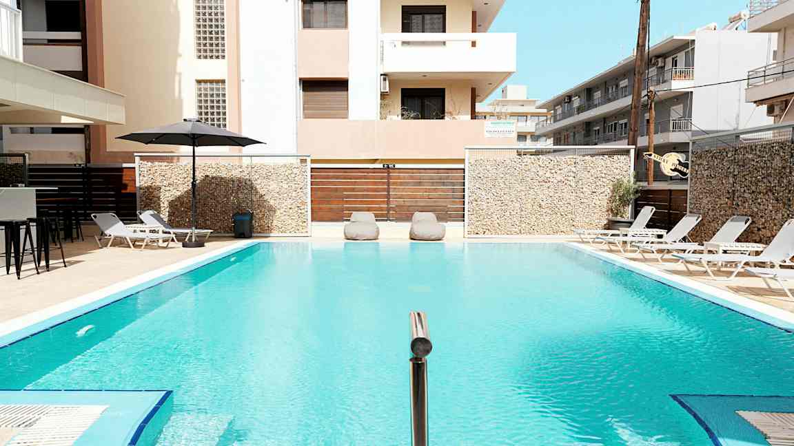 Et utendørs basseng omgitt av solsenger og bygninger. (AI-generert tekst)