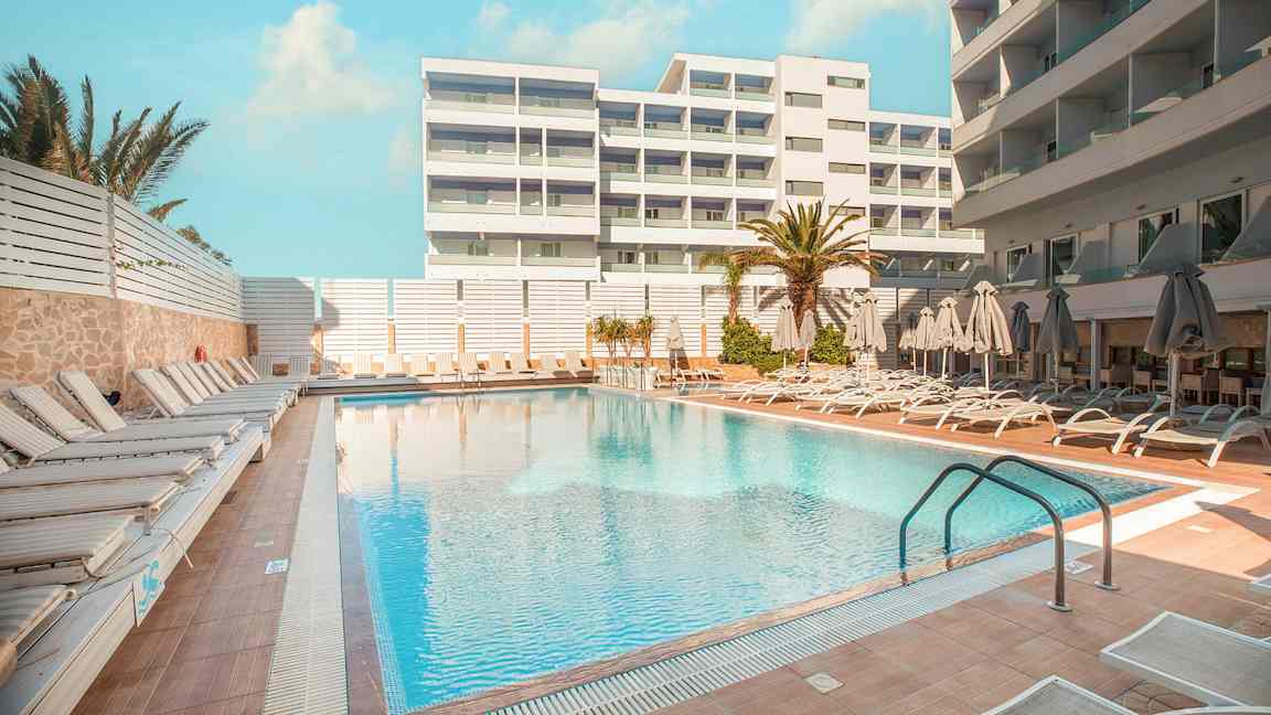 Hotellbasseng med solsenger og parasoller på omkringliggende terrasse. (AI-generert tekst)