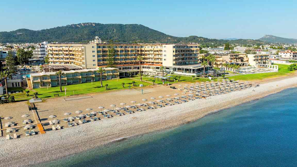 Hotellet ved stranden med solsenger og parasoller på sanden. (AI-generert tekst)