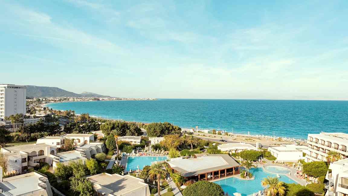 Utsikt over hotellområdet med bassenger og havet i bakgrunnen. (AI-generert tekst)