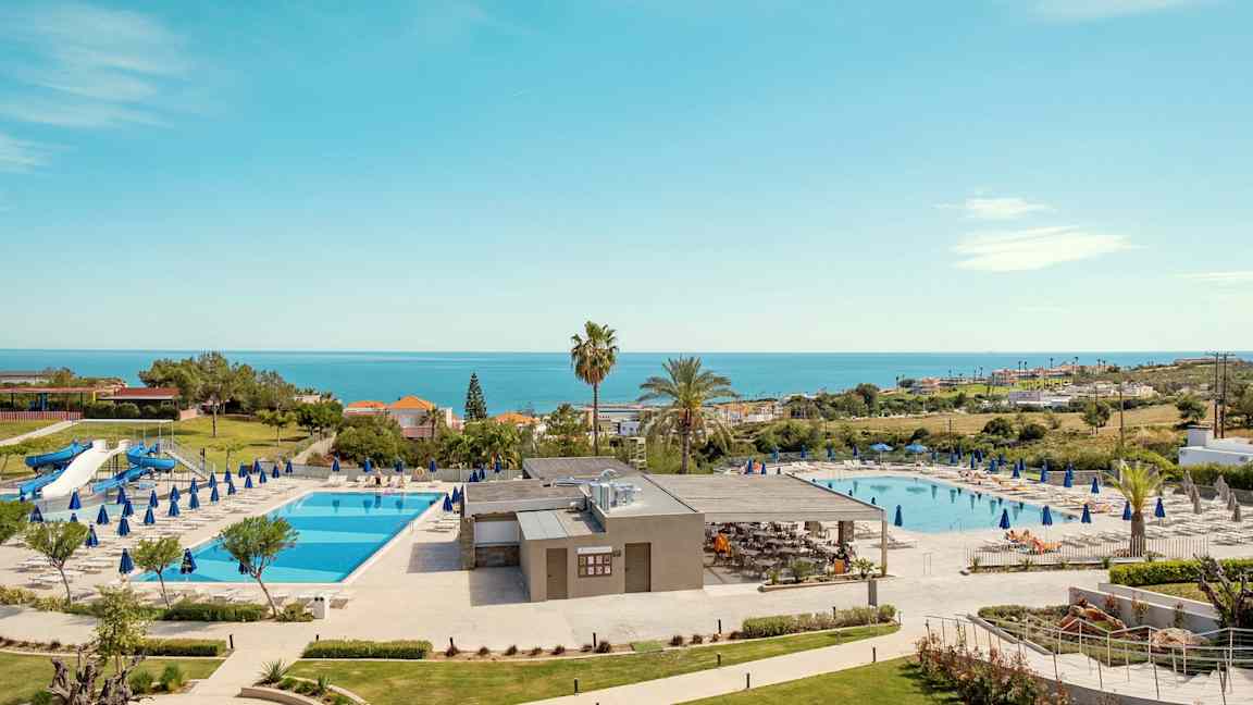 Hotellområde med to svømmebassenger, solsenger og havutsikt. (AI-generert tekst)