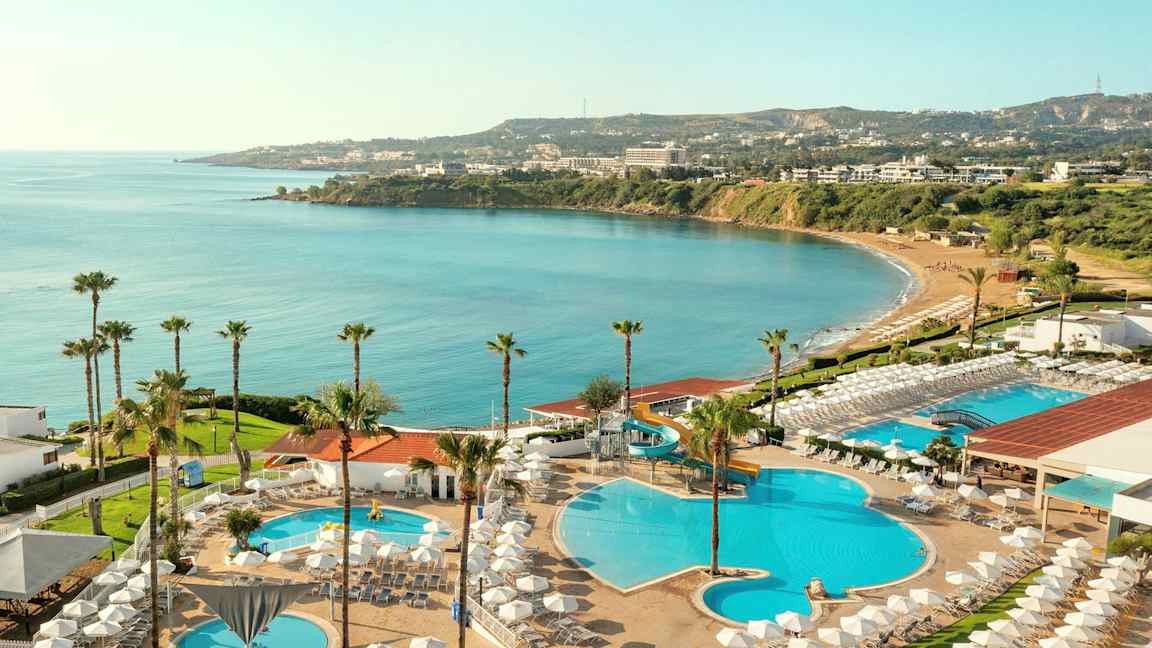 Utsikt over hotellområde med bassenger, solsenger og havutsikt. (AI-generert tekst)