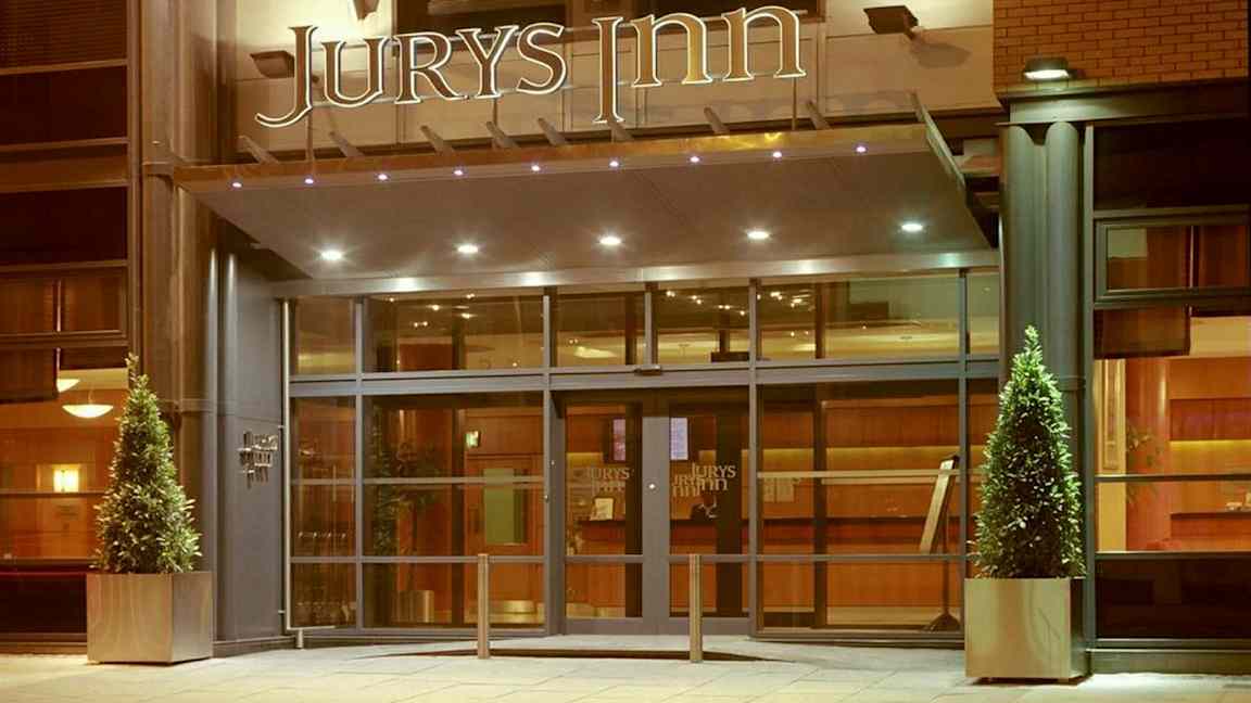 Hotellinngang med glassdører og skiltet 'Jurys Inn' over. (AI-generert tekst)