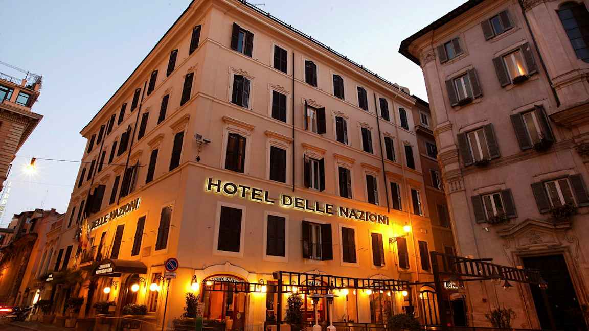 Bilde av en bygning med skilt som sier Hotel Delle Nazioni, opplyst med kveldssbelysning. (AI-generert tekst)