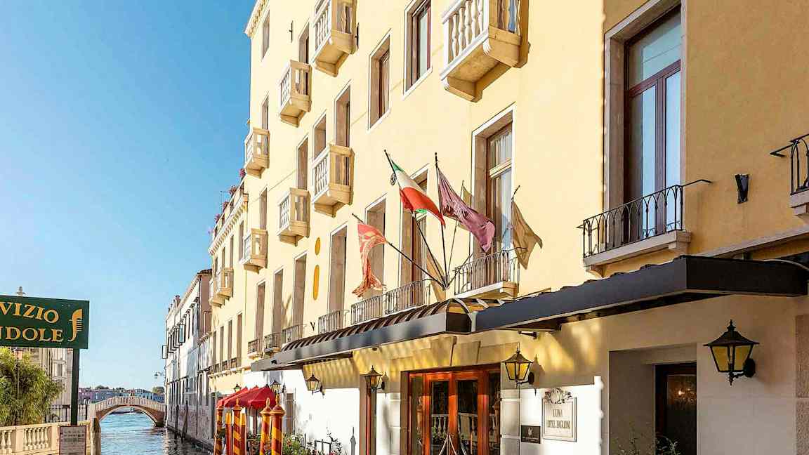 En gul bygning med balkonger langs en kanal, med en gangbro i bakgrunnen. (AI-generert tekst)