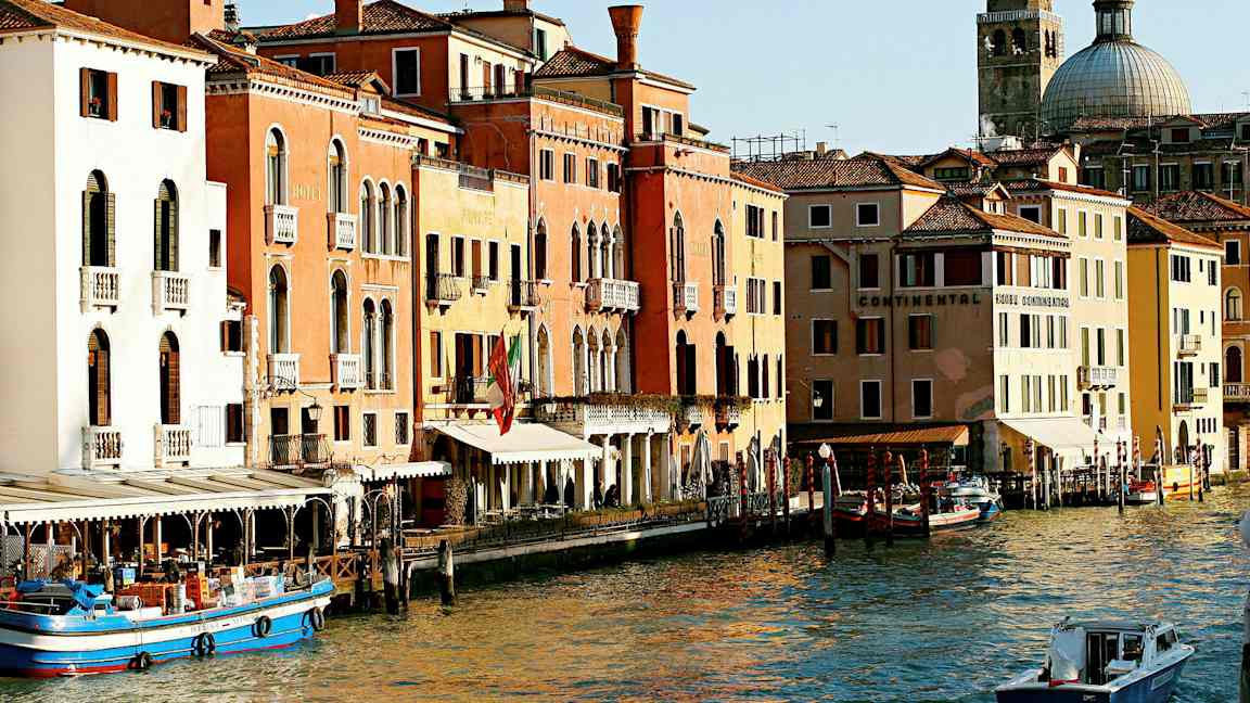 Et bilde av en kanal i Venezia med fargerike bygninger, båter og en kuppelformet kirke i bakgrunnen. (AI-generert tekst)