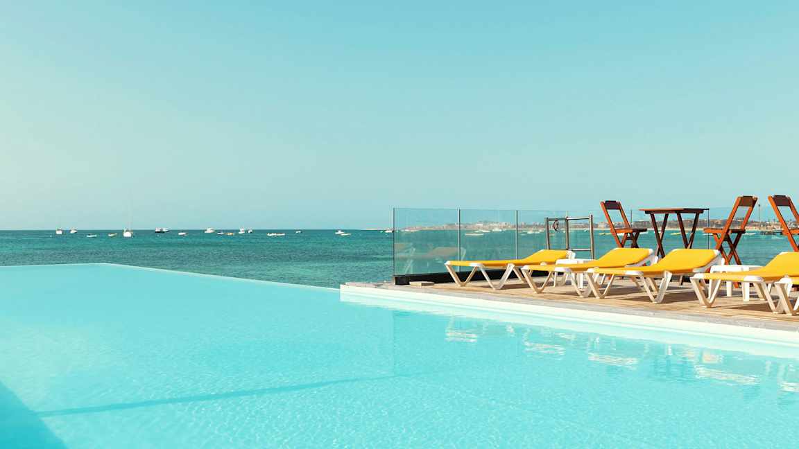 Svømmebasseng med utsikt over havet og solsenger ved siden. (AI-generert tekst)